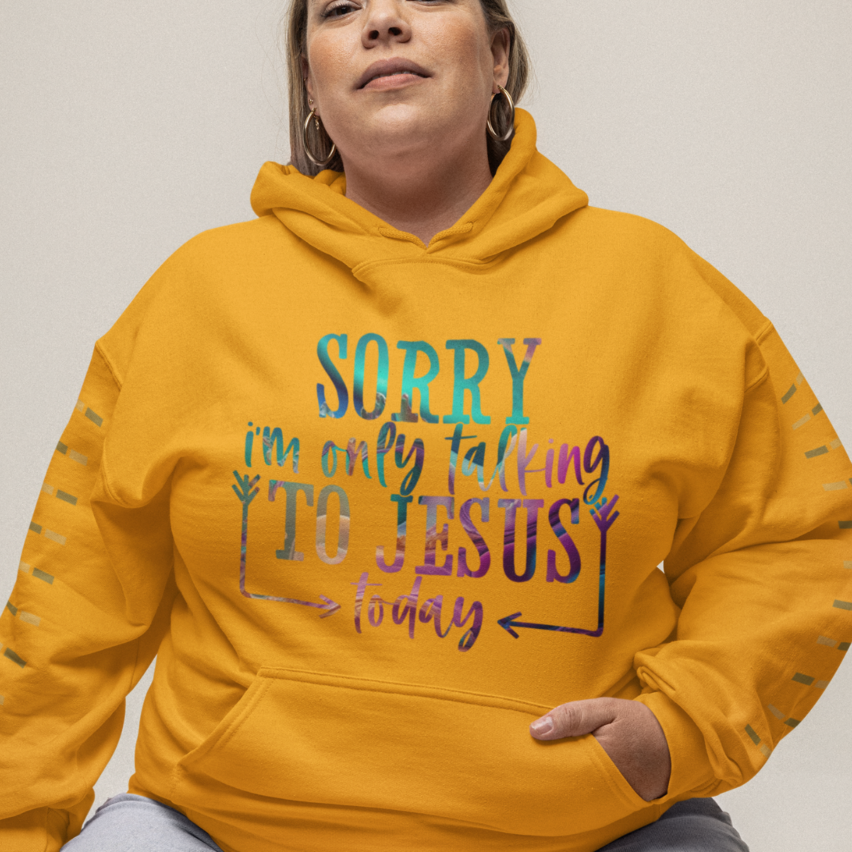 Woman wearing a gold hoodie with multicolor text 'SORRY i'm only talking TO JESUS today'.
